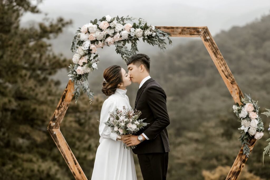 A romantic wedding scene with a couple kissing under a floral arch in a lush outdoor setting.